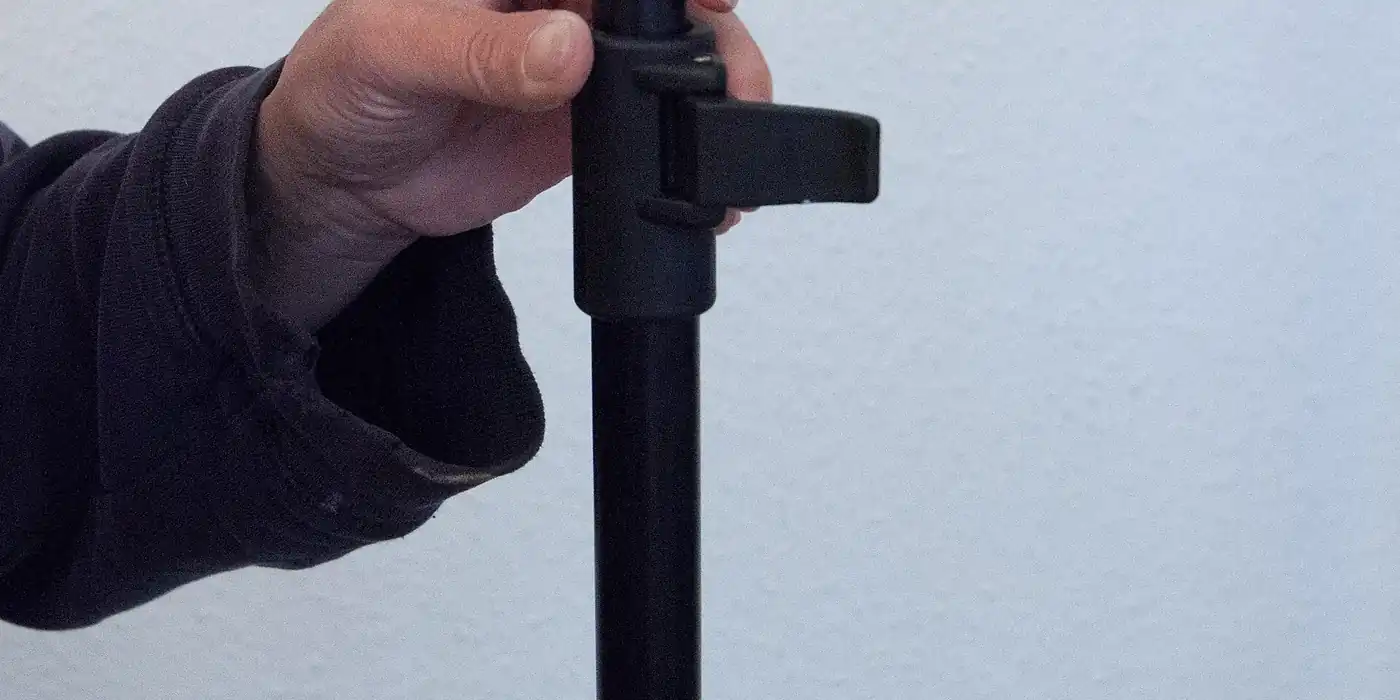 A hand tightening the clamp of a black lighting stand against a plain wall